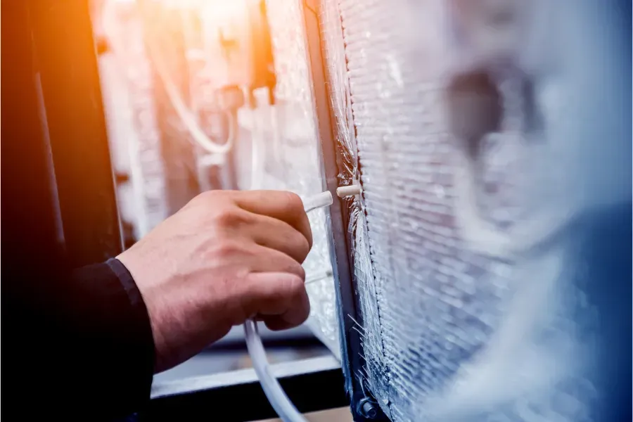 A technician flushing and cleaning an air conditioning drain line to prevent clogs and improve system airflow