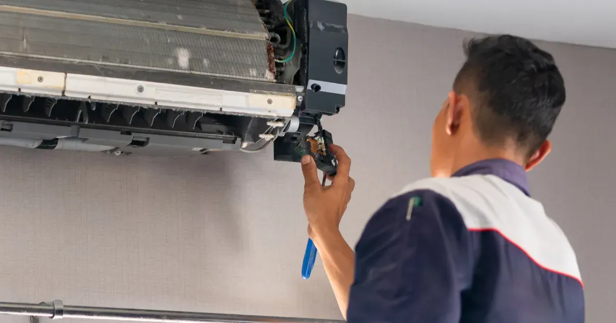 A technician carefully removes a faulty component from a wall-mounted air conditioning unit during a repair service