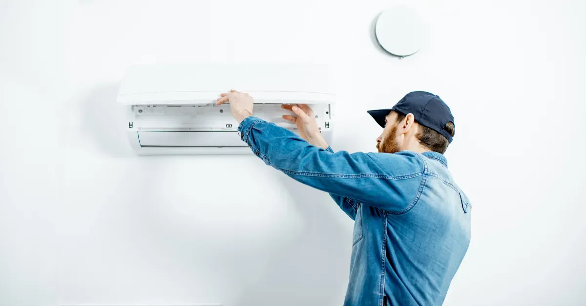A technician carefully opens the front panel of a wall-mounted air conditioning unit during routine maintenance