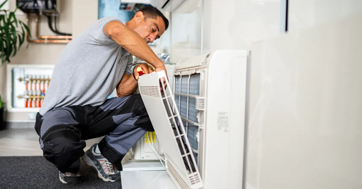 A technician is inspecting and cleaning an indoor air conditioning unit panel