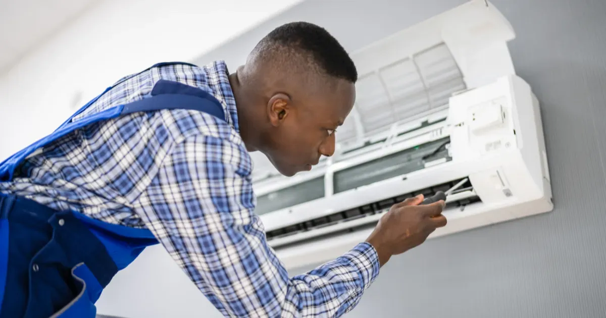 A technician in a blue uniform carefully inspects the internal components of a wall-mounted air conditioning unit