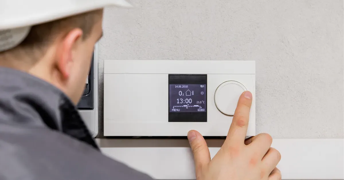 A technician adjusting a digital wall thermostat, setting temperature and system settings for indoor climate control