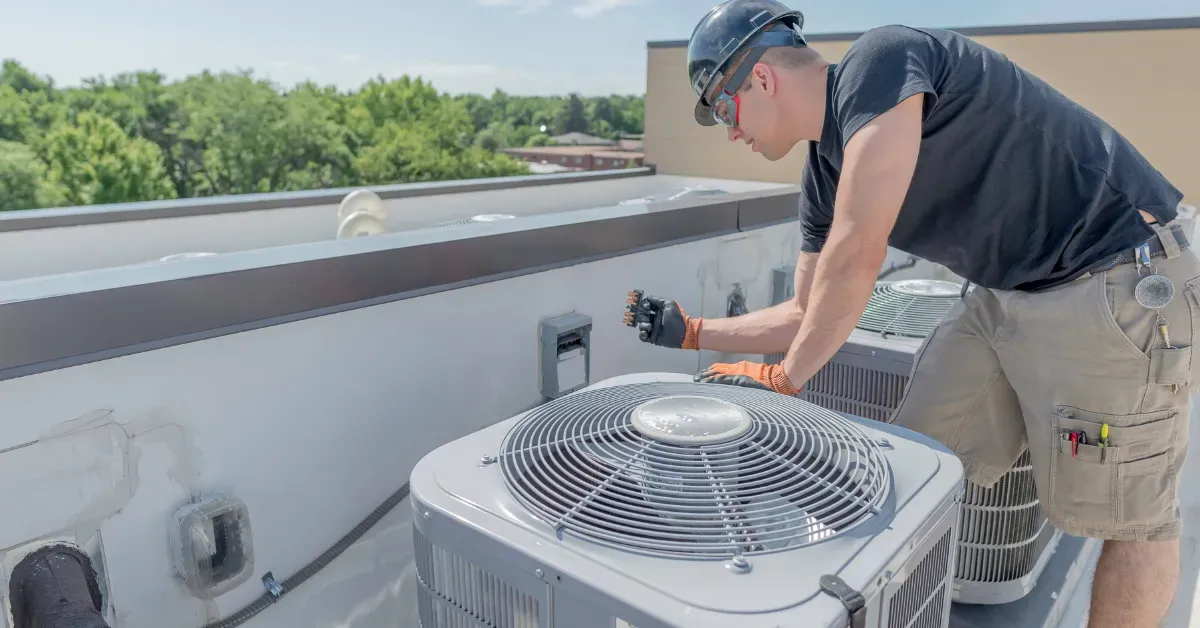 Person adjusting rooftop air conditioning unit with tools under clear daylight