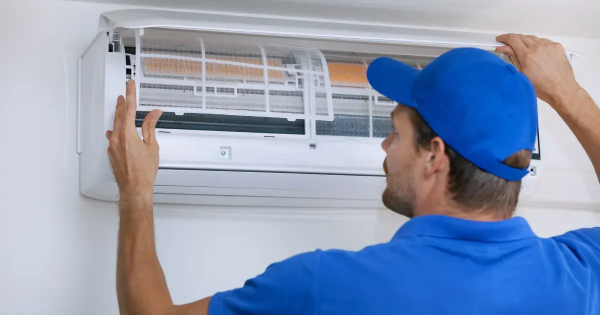 A technician in a blue uniform is opening the front panel of a AC unit